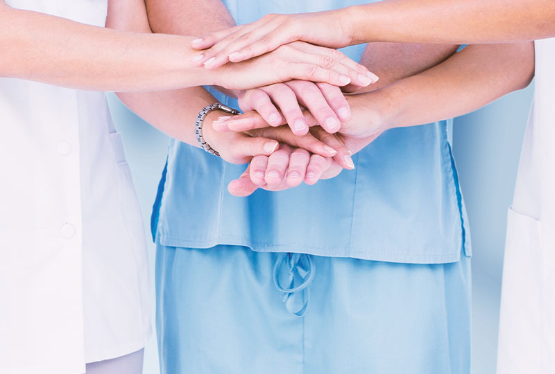 A group of five individuals, possibly dental professionals, in a dental office setting, celebrating with raised hands and thumbs up.