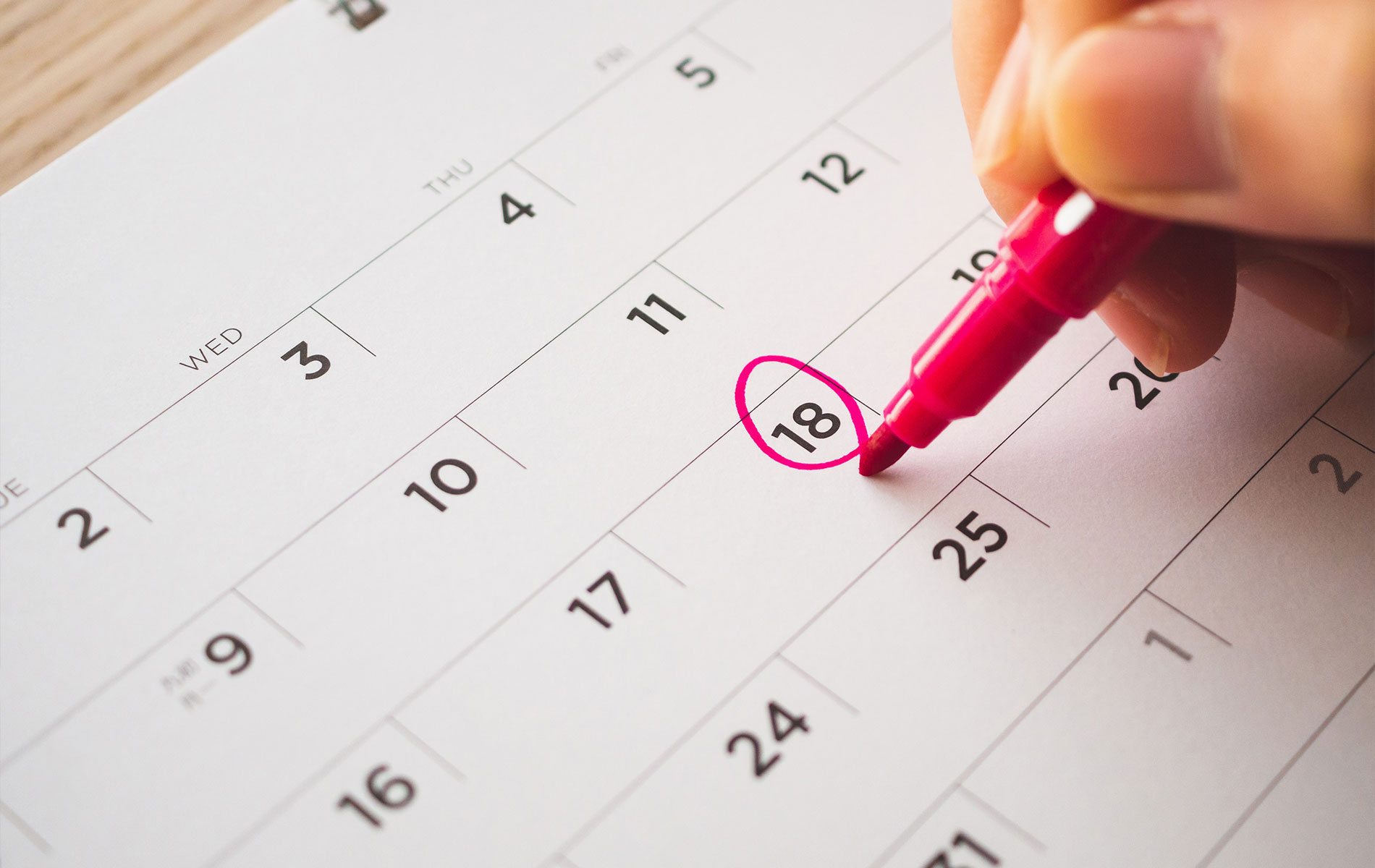 An alt tag for this image could be   A photograph depicting a hand marking the 18th day on a calendar with a red pen, signifying an important date.
