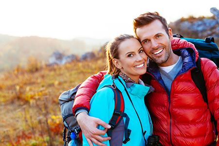 Two people embracing outdoors, posing with backpacks against scenic backdrop.