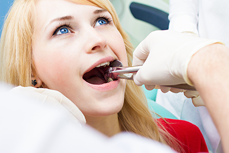 A dental professional adjusting a woman s teeth with a dental tool.