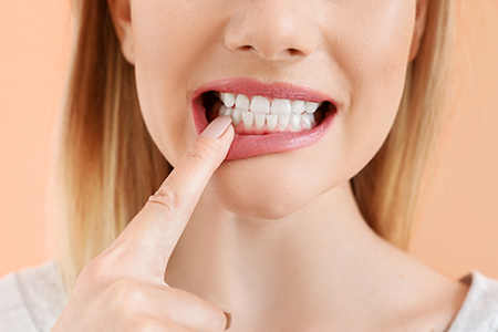Woman with her finger on her teeth, possibly brushing or cleaning them.