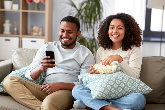 Two people sitting on a couch, enjoying a movie together with snacks.